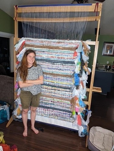 MSU Anthropology PhD candidate and local artist Kelsey Merreck Wagner stands with her tapestry she wove using plastic. For more of her art, visit her website. Photo credit: Kelsey Merreck Wagner. 